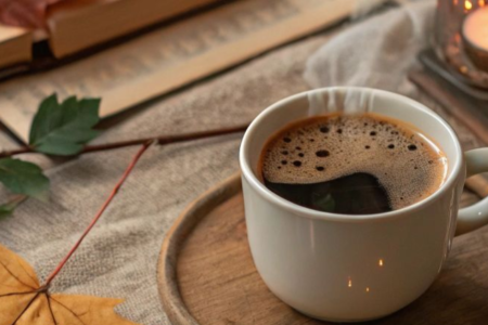 A cup of coffee with autumn leaves and a candle light