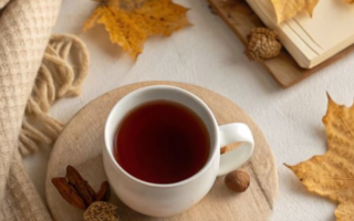 A cup of coffee , an autum leaf, a cream blanket and a book