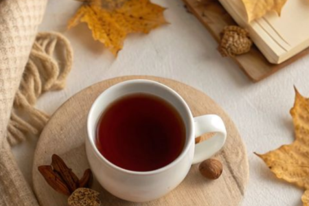 A cup of coffee , an autum leaf, a cream blanket and a book