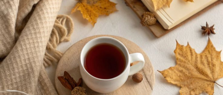 A cup of coffee , an autum leaf, a cream blanket and a book